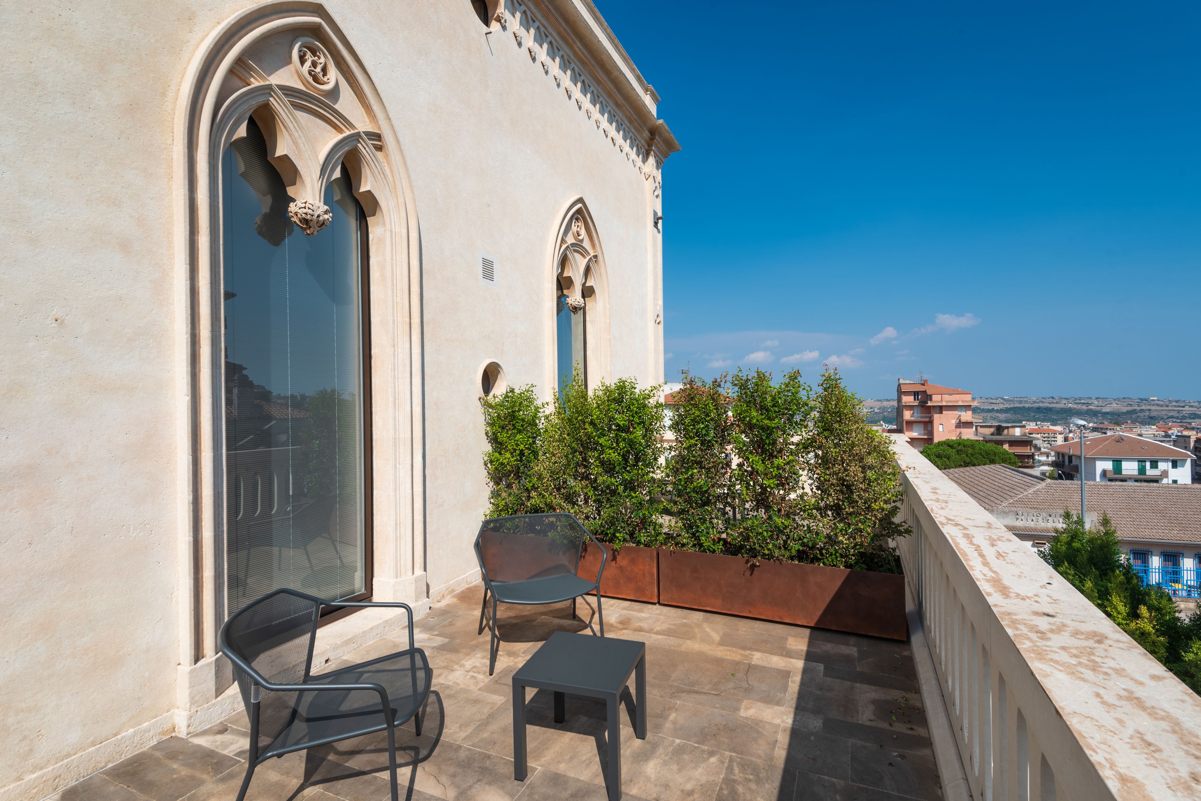 A balcony with two chairs and a small table, overlooking a cityscape.