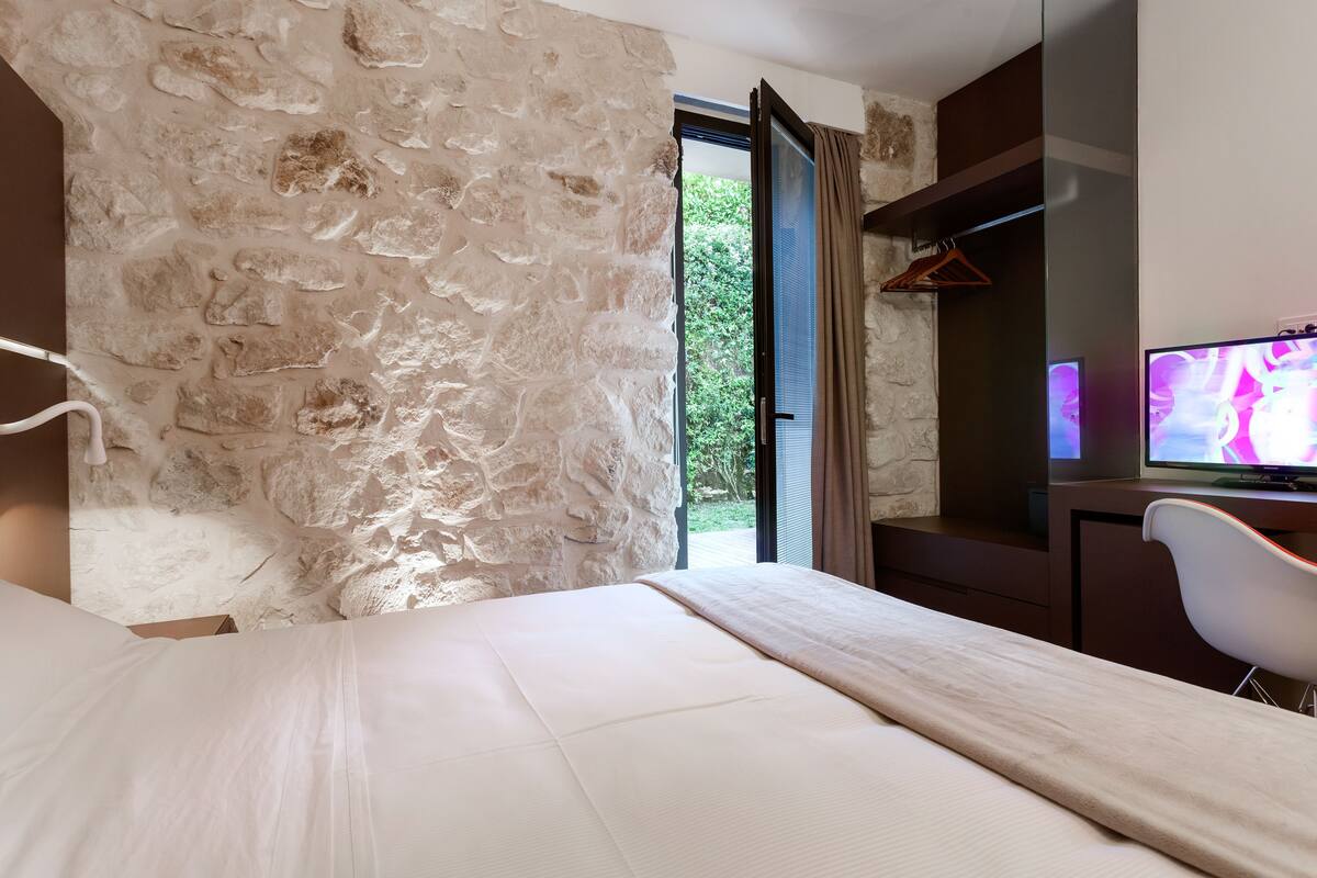 Une chambre avec un mur en pierre, un lit, un bureau avec une chaise et un téléviseur.