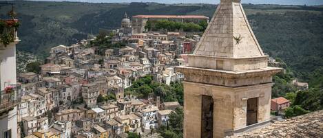 A historic town with a prominent bell tower, dense architecture, and a hillside backdrop.