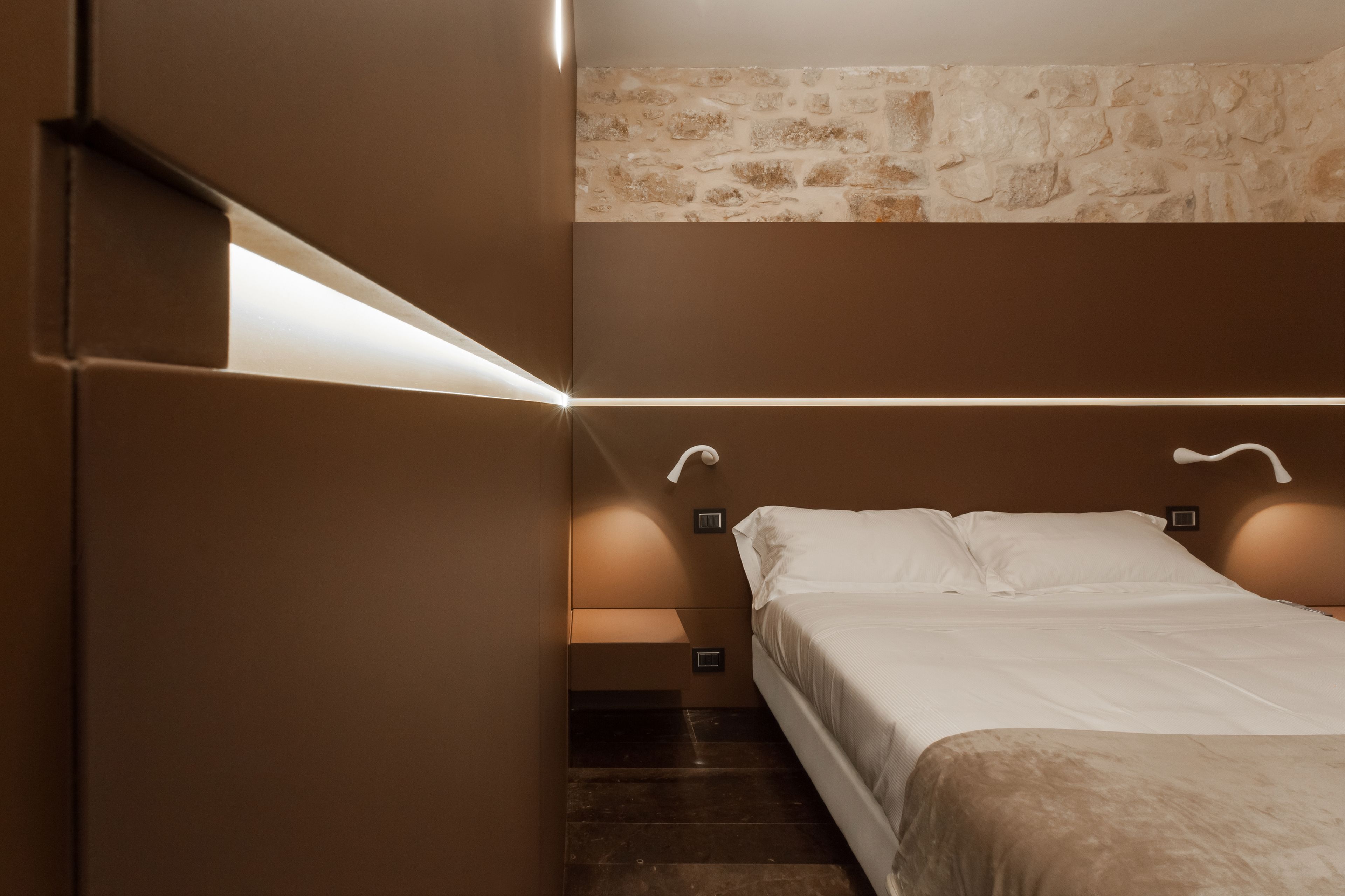 A bedroom with a bed, a stone wall, and built-in lighting.