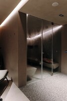 Een moderne lift met glazen deur, een bankje binnenin, en een bedieningspaneel met knoppen.