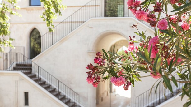Un escalier de marbre menant à une porte en arc de cercle, entourée de fleurs roses.