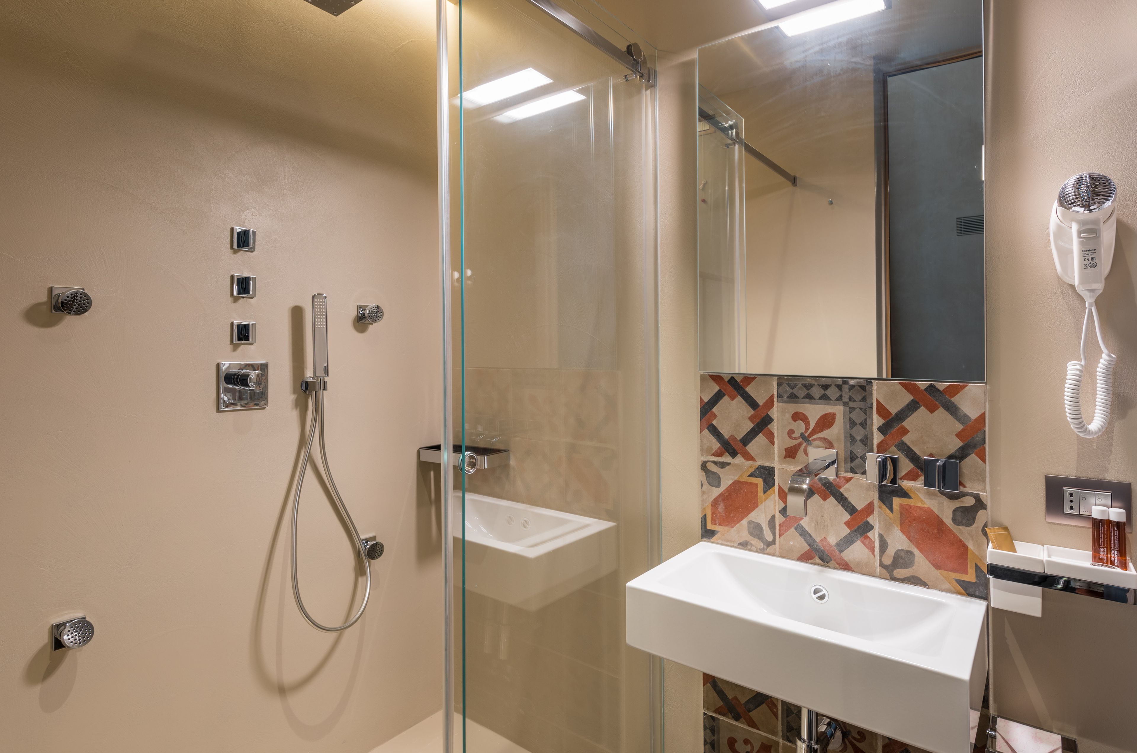 Un baño moderno con cabina de ducha de vidrio, un lavamanos blanco y un secador de pelo fijado en la pared.