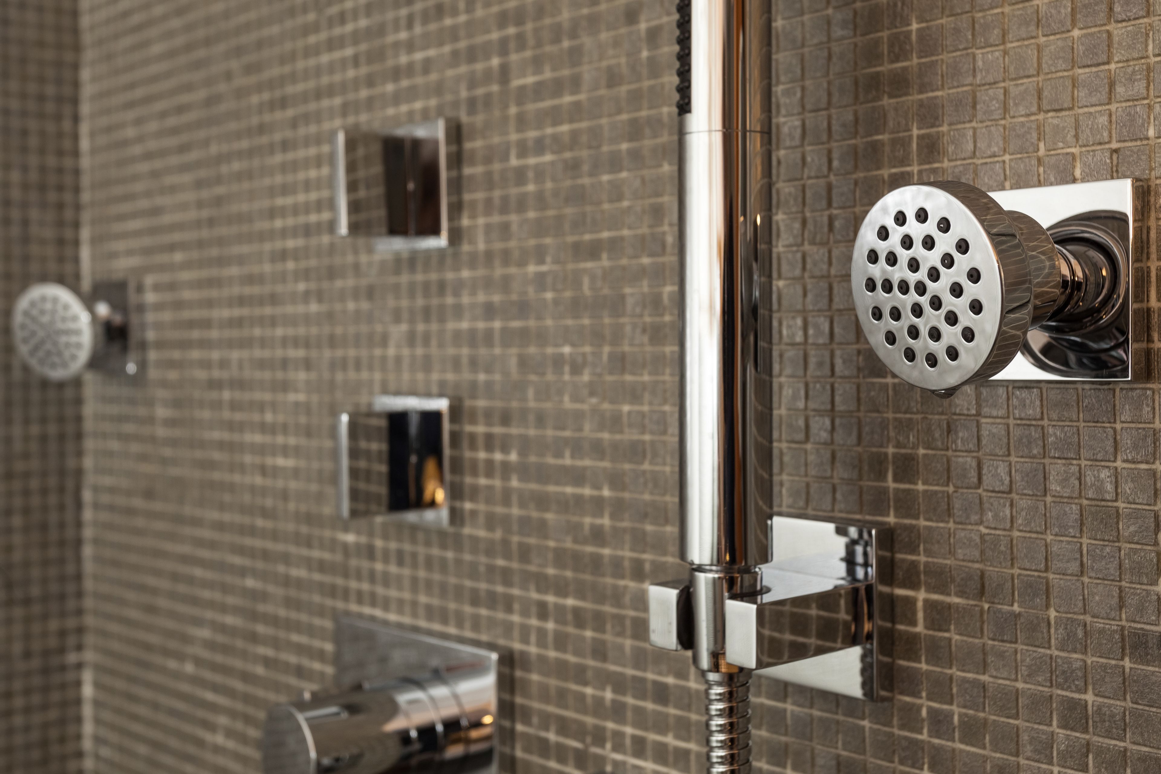 Un baño con pared de azulejos, un cabezal de ducha y una ducha de mano.