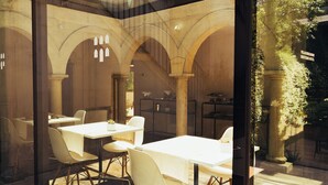 Un espace repas entièrement vitré, avec des tables et des chaises blanches, des arches en pierre et une vue sur le jardin extérieur.