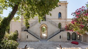 Une cour intérieure avec un escalier central menant à une entrée en arc de cercle, le tout entouré de murs de pierre et de verdure.