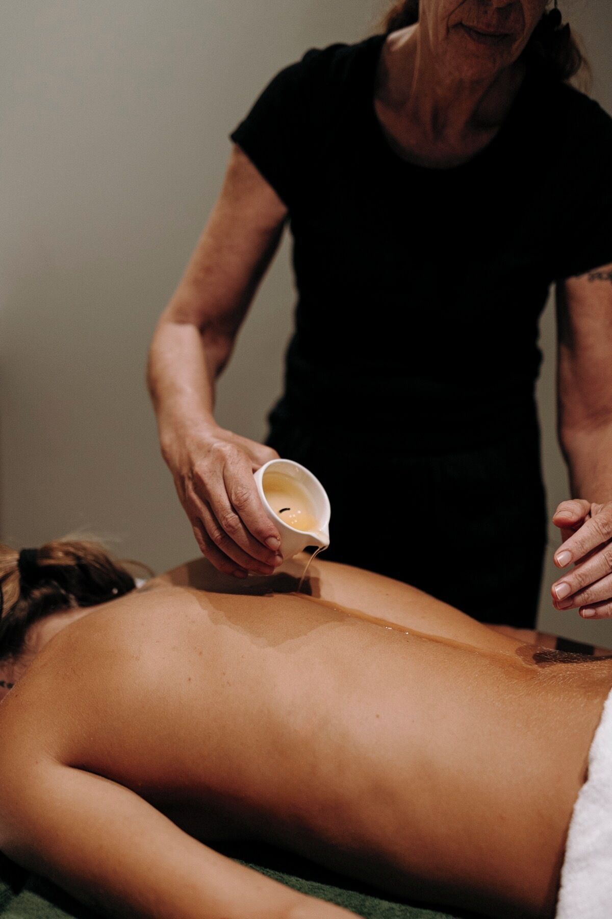 A person receiving a massage with a cup of oil being poured on their back.