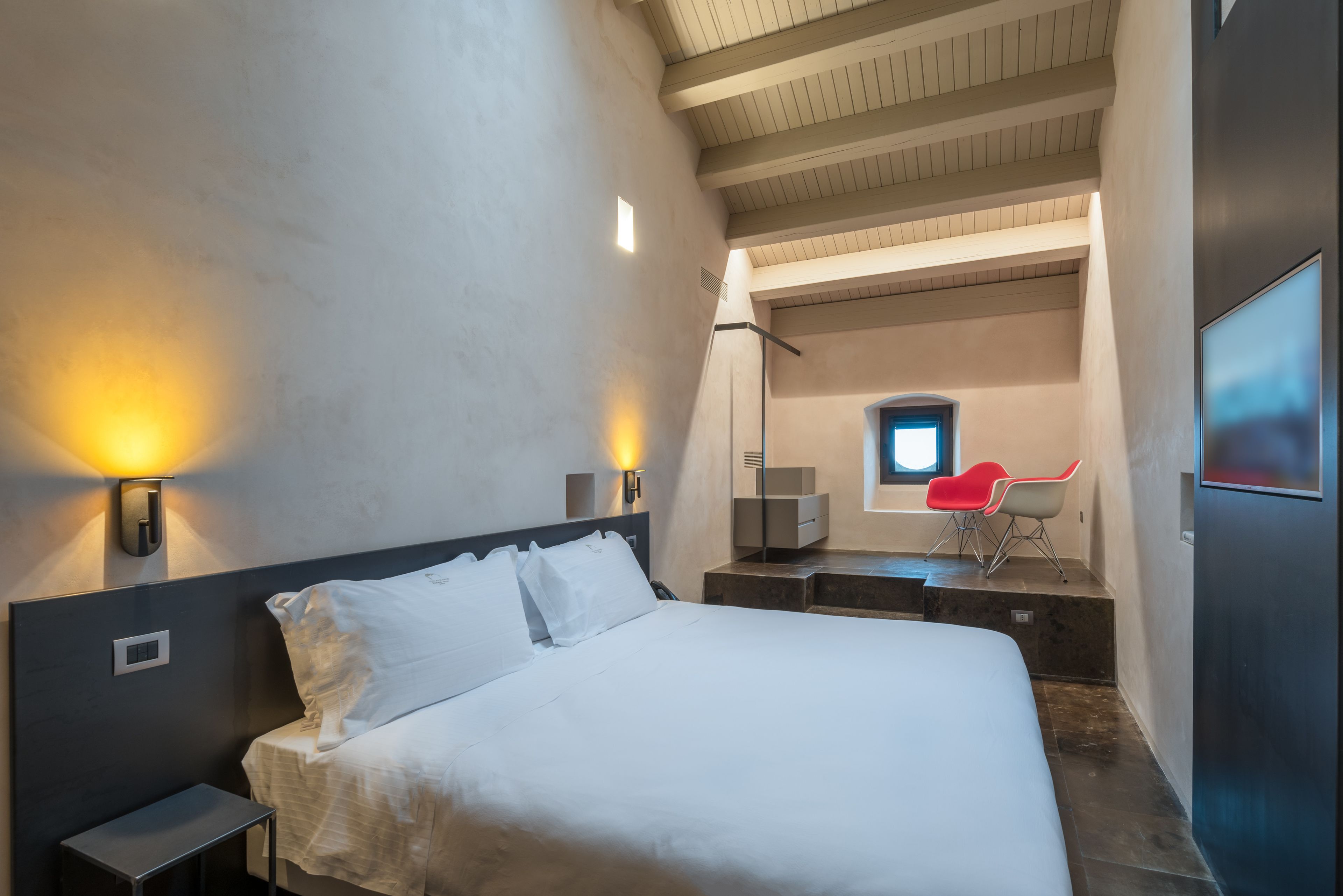 Una habitación de hotel moderna con una cama grande, mesitas de noche, un escritorio y una silla. Hay una ventana que ofrece vistas al exterior.