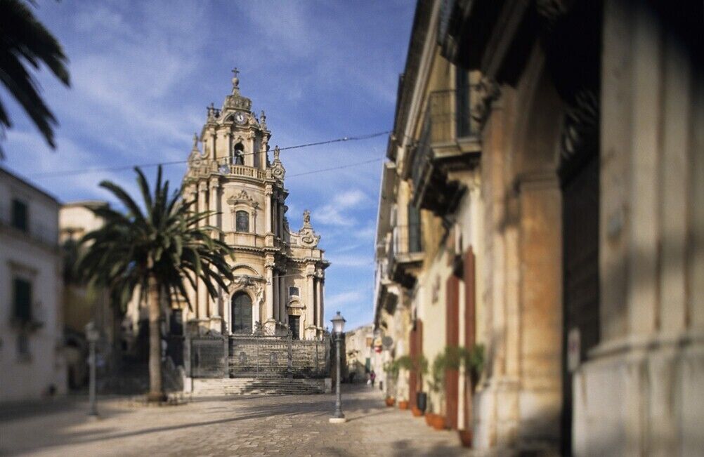 A street leading to a historic church with ornate architecture, palm trees, and buildings on either side.