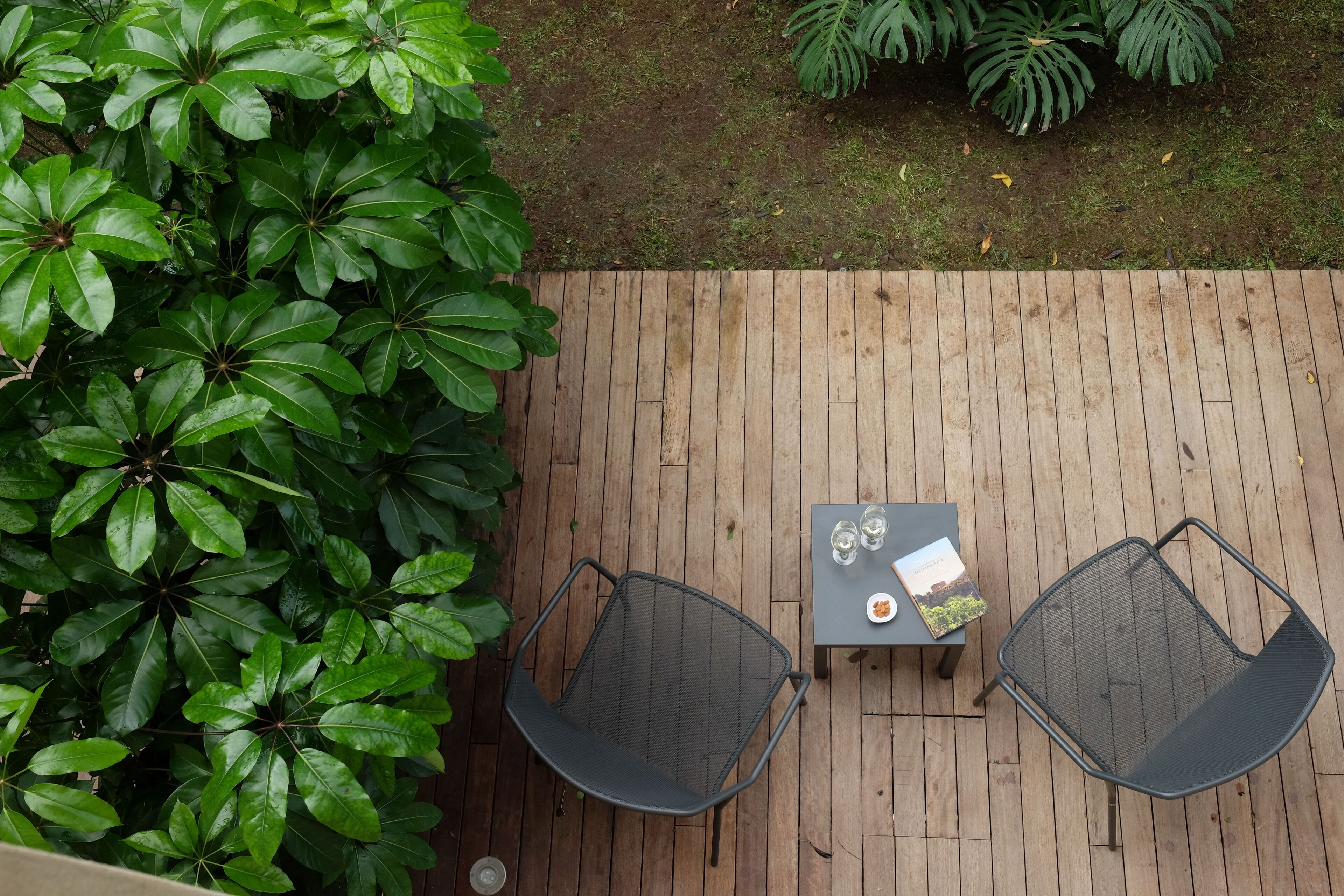 Une terrasse extérieure en bois, agrémentée de deux chaises en métal et d’une table, le tout entouré d’un luxuriant feuillage verdoyant.