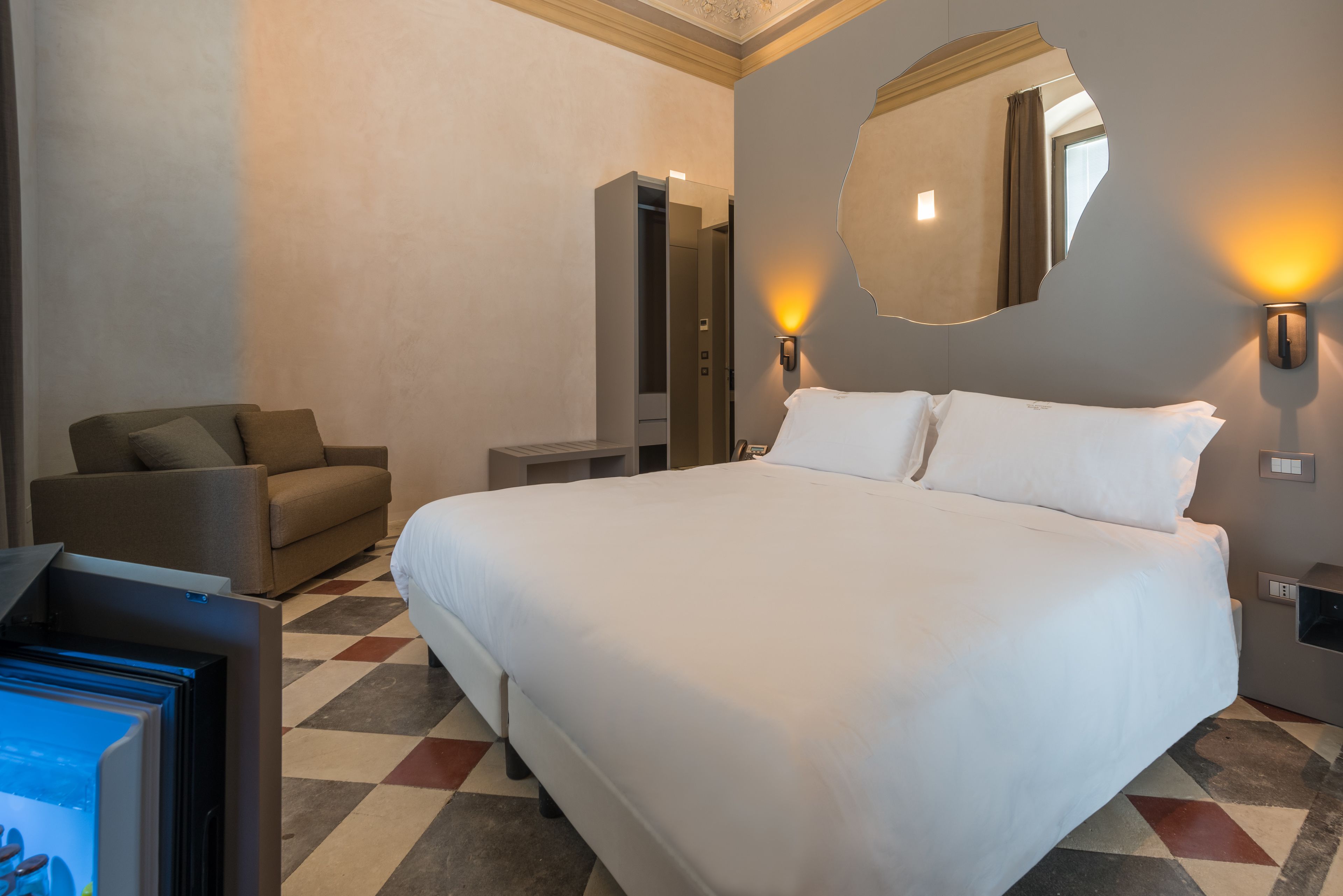 Una habitación de hotel con una cama grande, un sofá, un televisor y un espejo en la pared.