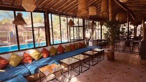 Una zona de estar junto a la piscina con un sofá azul, cojines de colores y mesas de metal.