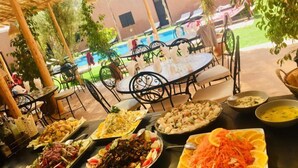 Un área de comedor al aire libre con mesas y sillas, una piscina al fondo y varios platos de comida sobre las mesas.