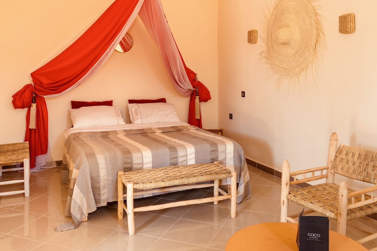 A bedroom with a canopy bed, a woven bench, and a wicker chair.