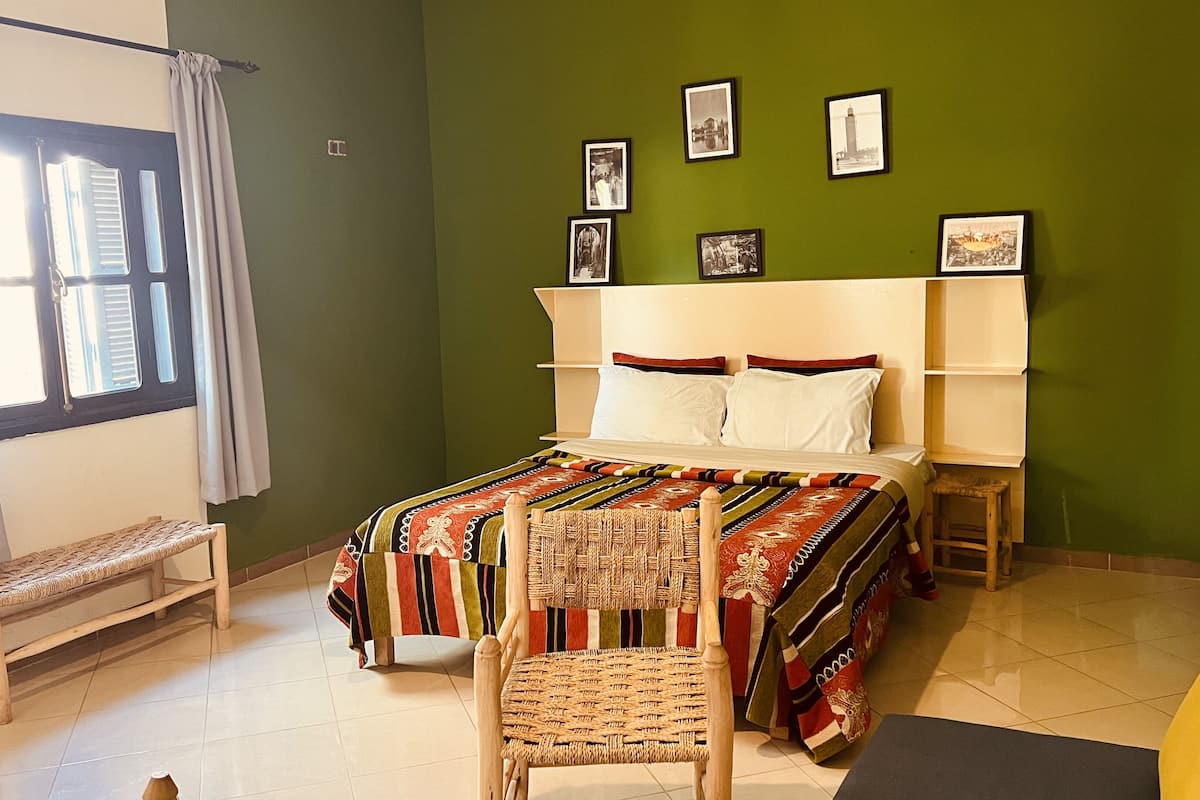 A bedroom with a bed, a bench, a chair, and a wall with framed pictures.