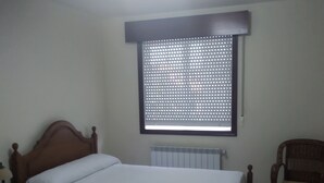 A room with two single beds, a wooden chair, a radiator, and a window with a metal screen. - Hostal El Viejo Galeón (Baiona)