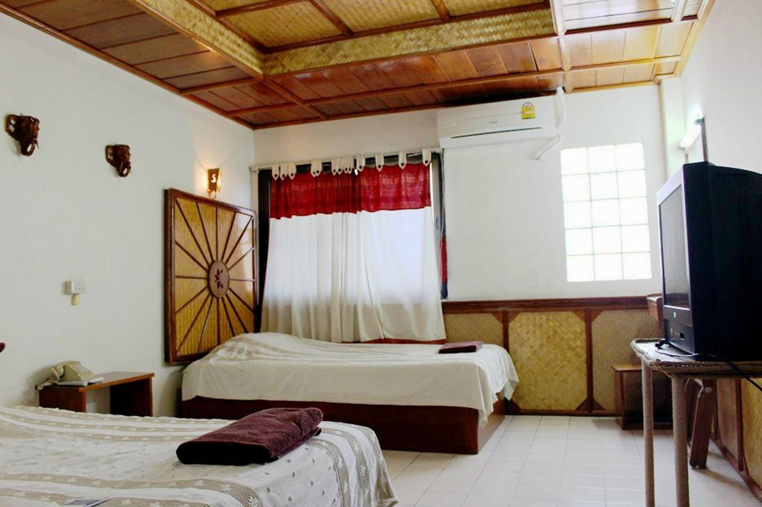 A hotel room with two beds, a television, an air conditioning unit, and a decorative wall piece.