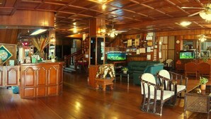 A spacious lobby with wooden flooring, a reception desk, seating area, and a television.