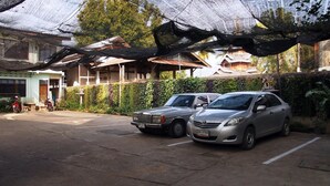 A parking area with two cars, a building with a green wall, and a traditional structure in the background.