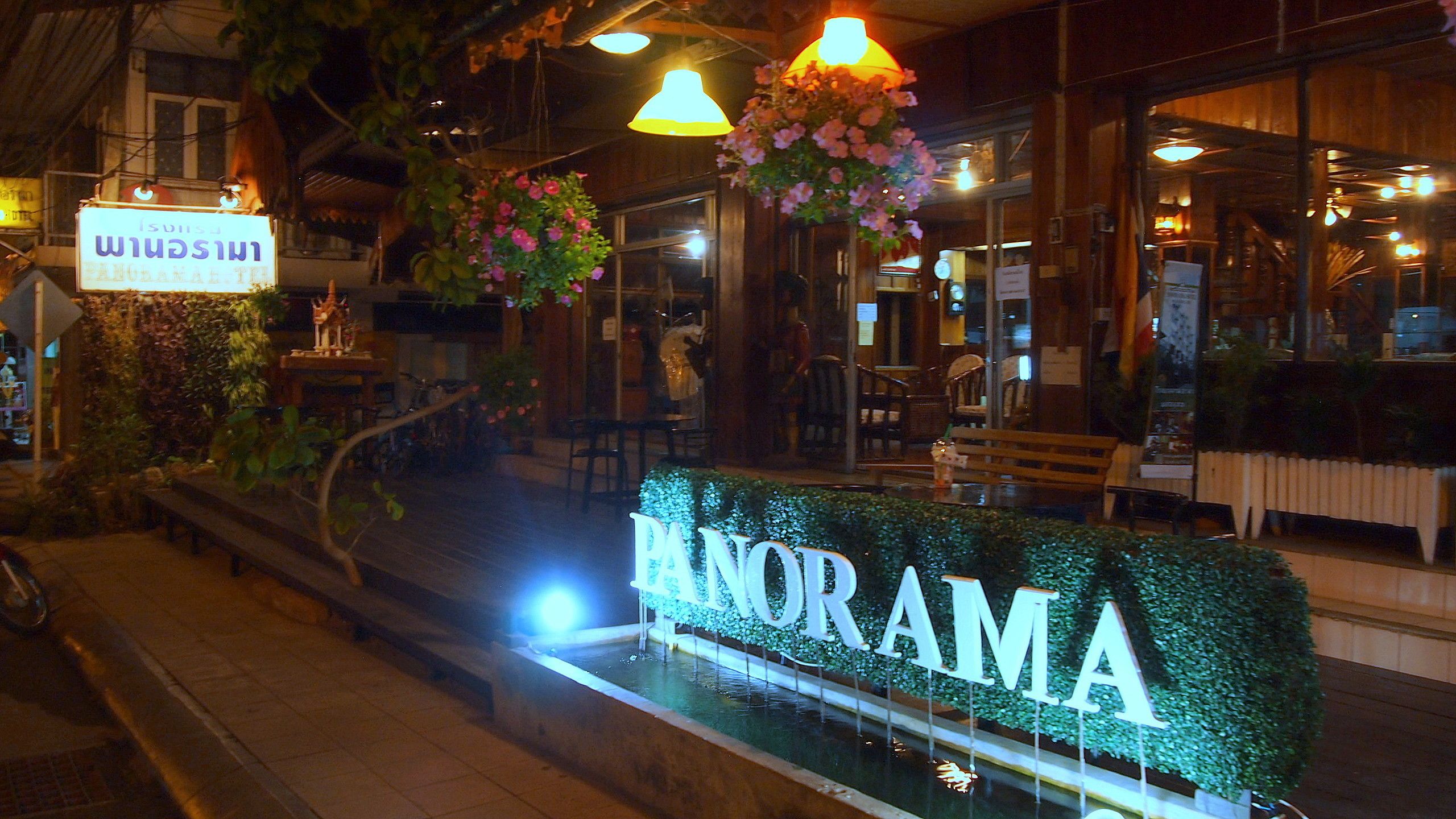 A restaurant named 'PANORAMA' with a water feature in front, outdoor seating, and hanging flower baskets.