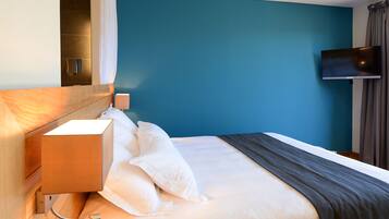 Une chambre d’hôtel avec un lit, une table de chevet, un téléviseur fixé au mur et un rideau.