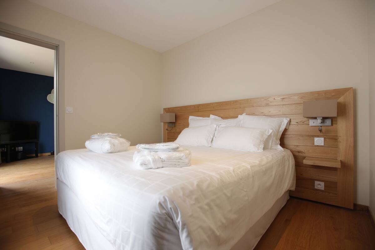 Un lit bien fait, avec du linge de lit et des serviettes blanches, une tête de lit en bois et des lampes de chevet.