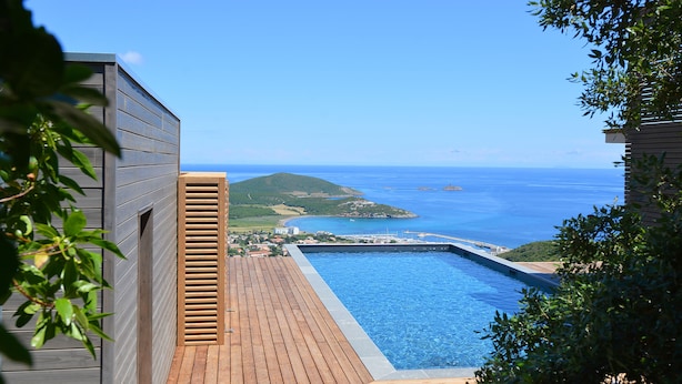 A wooden deck leading to a pool with a view of the sea and a distant island. - Hotel le Tomino (Tomino)