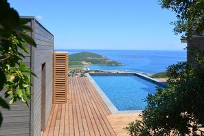 Une terrasse en bois qui mène à une piscine, offrant une vue sur la mer et une île lointaine.