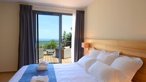A hotel room with a large bed, a wooden headboard, a balcony with a view of the ocean, and a table with chairs outside. - Hotel le Tomino (Tomino)