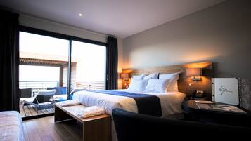 A modern hotel room with a large bed, a desk, a chair, and a balcony with a view.