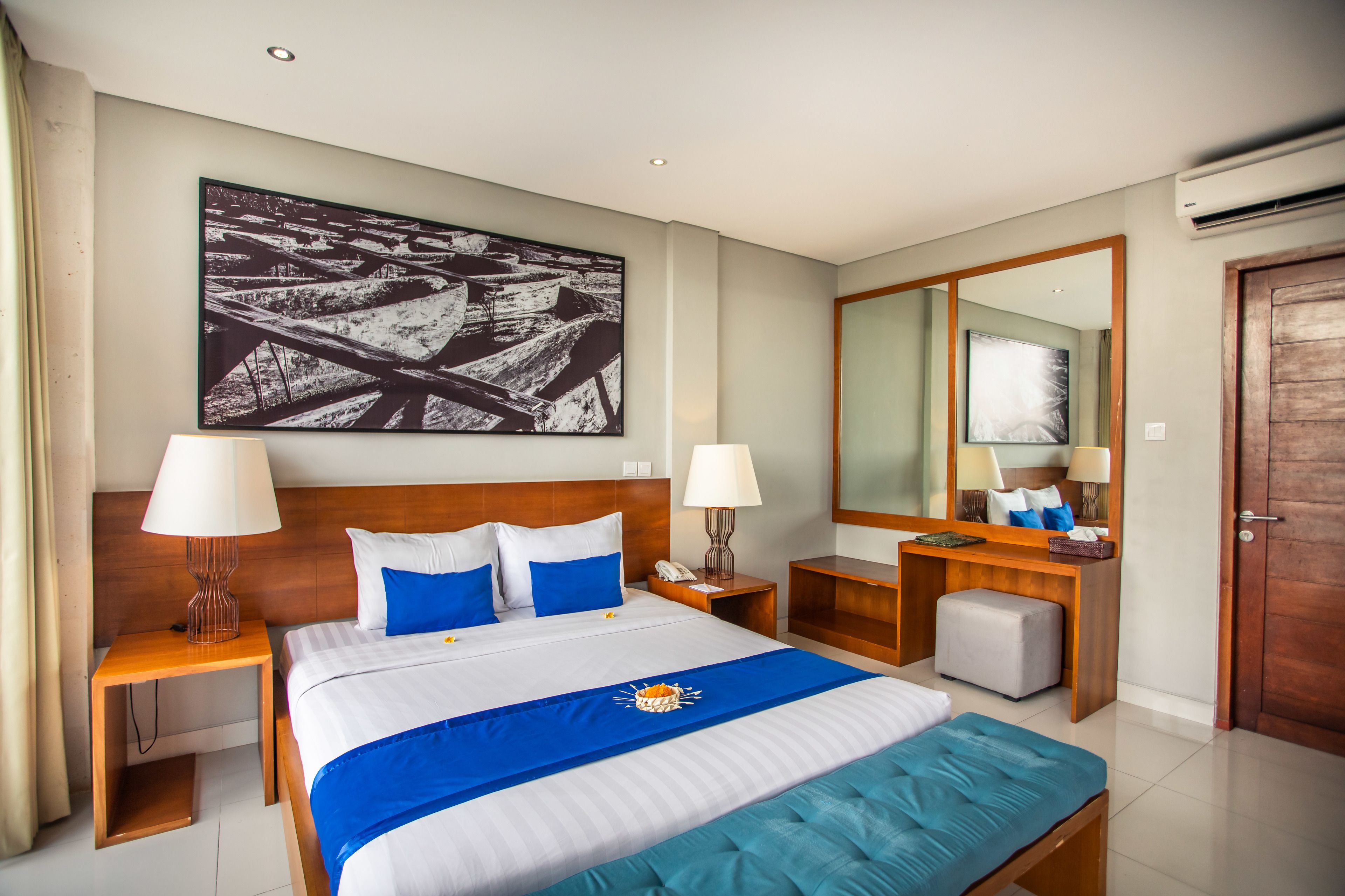 A hotel room with a large bed, two bedside tables, a desk, a chair, a mirror, and a door.