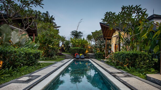 A rectangular swimming pool with a tiled border, surrounded by lush greenery and tropical plants. - Bakung Ubud Resort and Villa (Ubud)
