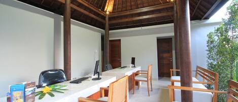 Un área de recepción con un mostrador de madera, dos sillas de madera, una computadora y una planta.