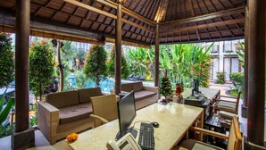 A covered outdoor seating area with a pool view, featuring a sofa, dining table, and computer setup. - Bakung Ubud Resort and Villa (Ubud)