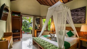 A bedroom with a canopy bed, a bedside table with a lamp, a green bench, a wardrobe, and a television on the wall. - Bakung Ubud Resort and Villa (Ubud)