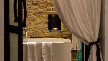 A bathroom with a stone wall, a bathtub, and two towels hanging on the wall.