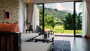 A bedroom with a large window, a stone wall, and a view of a green landscape. - The Pavilions Himalayas The Farm (Pokhara)