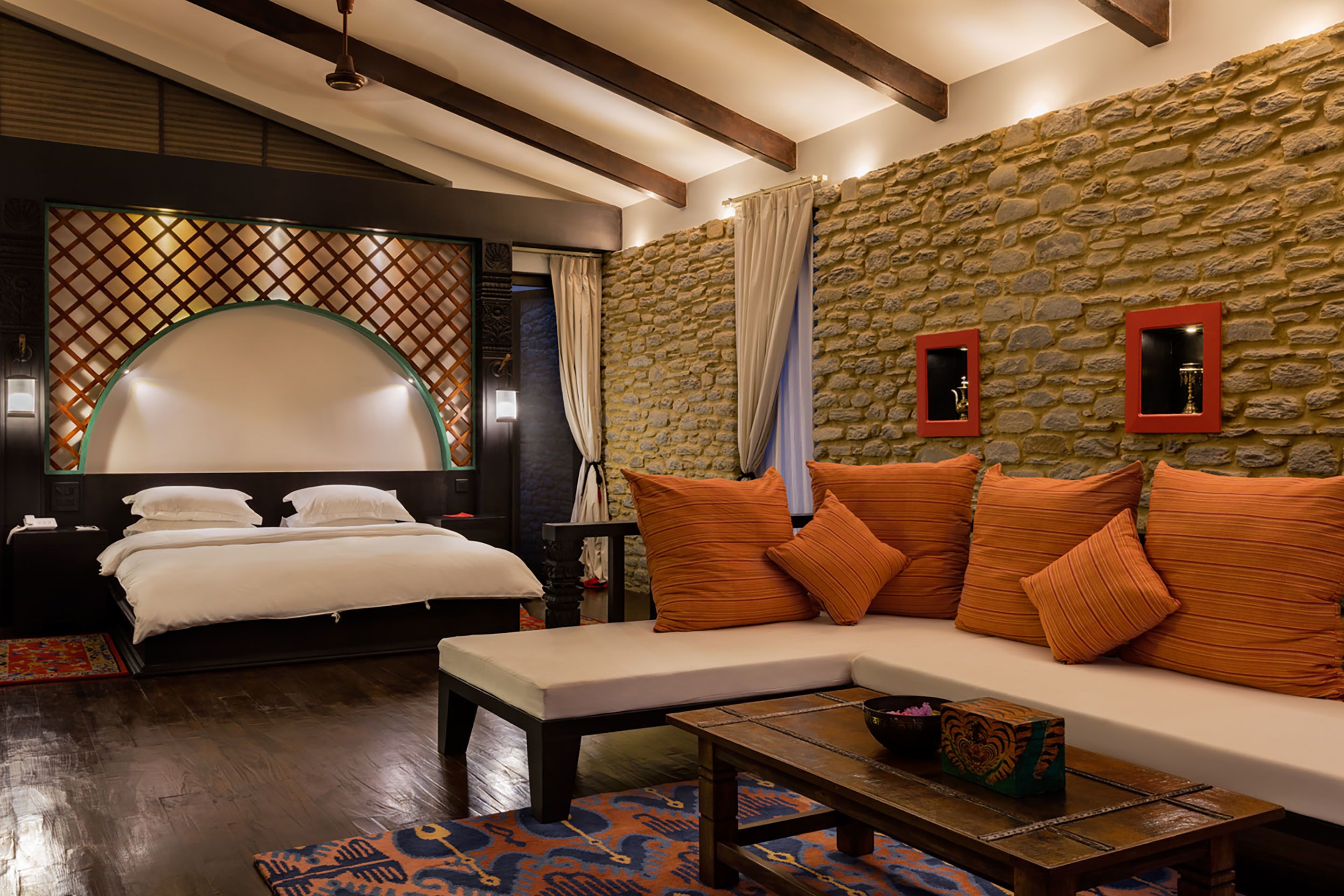Une chambre d’hôtel avec un grand lit, un canapé, une petite table et un mur en pierre.
