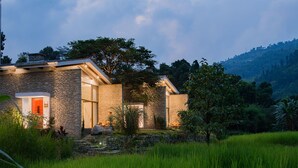 A stone house with a red door, surrounded by lush greenery and a hilly landscape. - The Pavilions Himalayas The Farm (Pokhara)