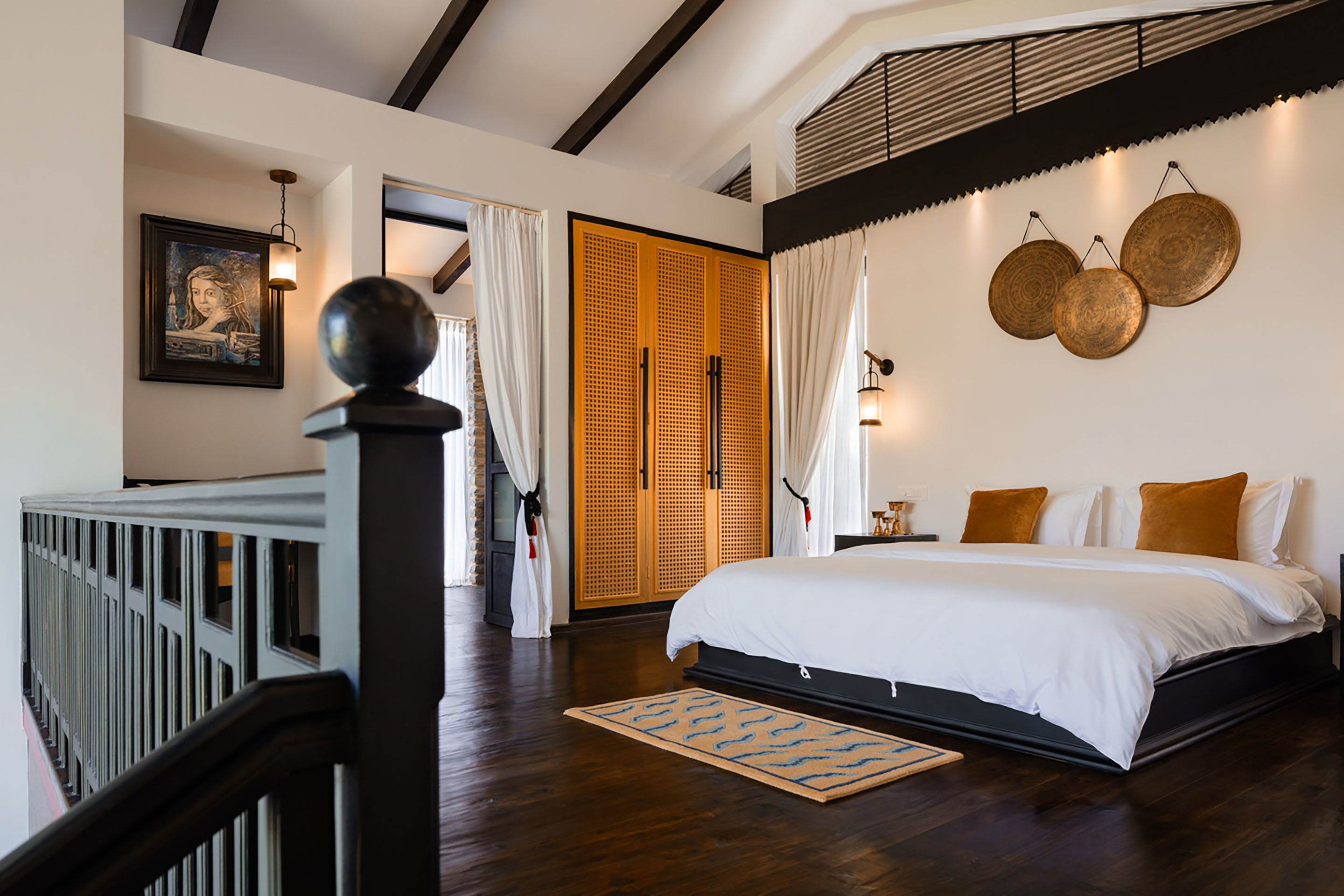 A bedroom with a large bed, wooden flooring, a view of the outdoors, and a staircase.