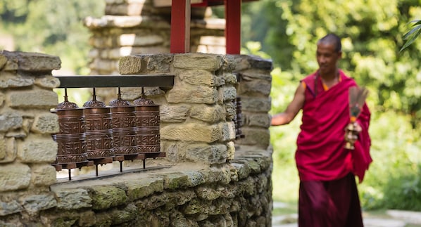 Une structure en pierre surmontée d’un objet métallique, peut-être un artefact religieux, et une personne vêtue d’une robe rouge en arrière-plan.