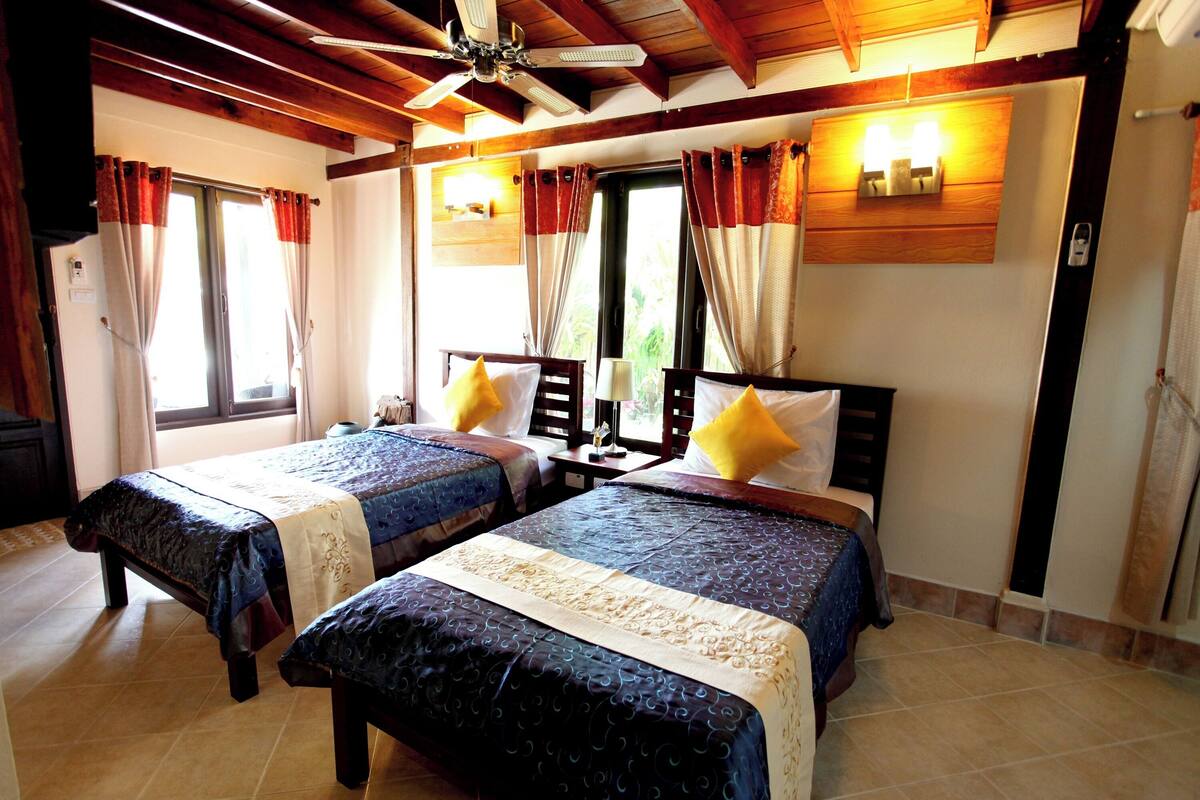 A room with two beds, a ceiling fan, and a window with curtains.