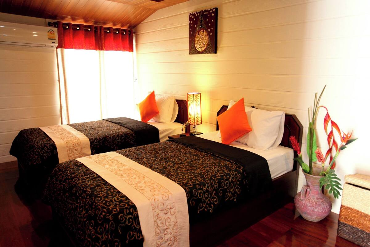 A hotel room with two beds, a nightstand with a lamp, a decorative wall piece, and a potted plant.