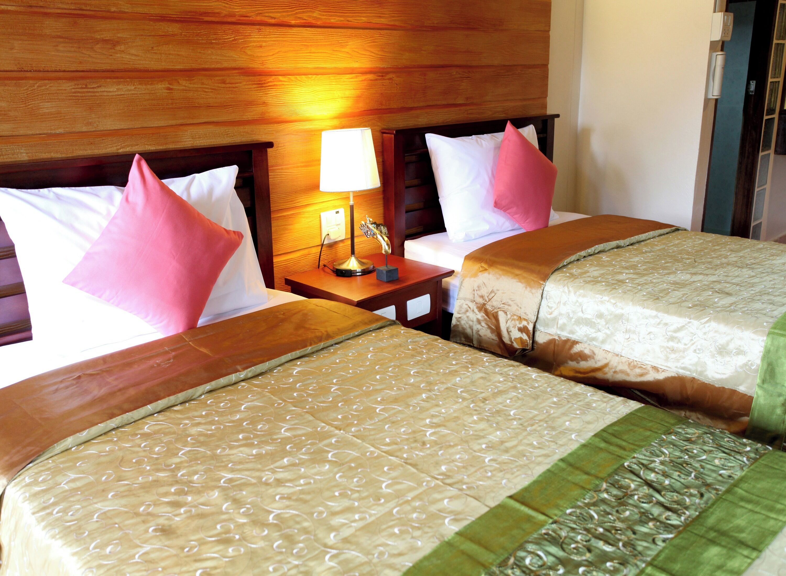 A hotel room with two beds, wooden headboards, a nightstand with a lamp, and a window with curtains.