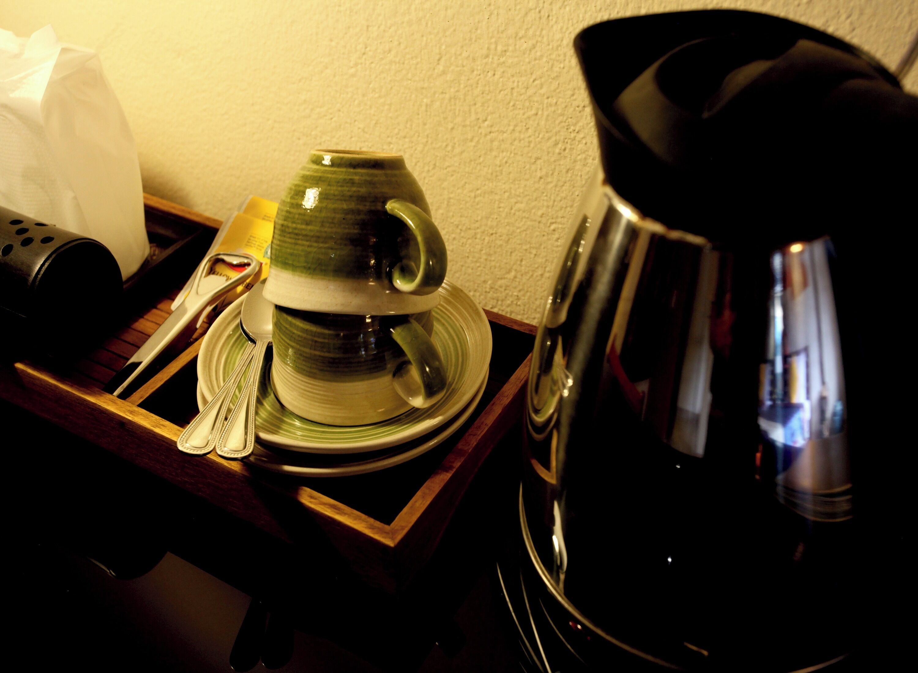 Una bandeja con una taza de cerámica, una cuchara, una servilleta y una tetera eléctrica negra.