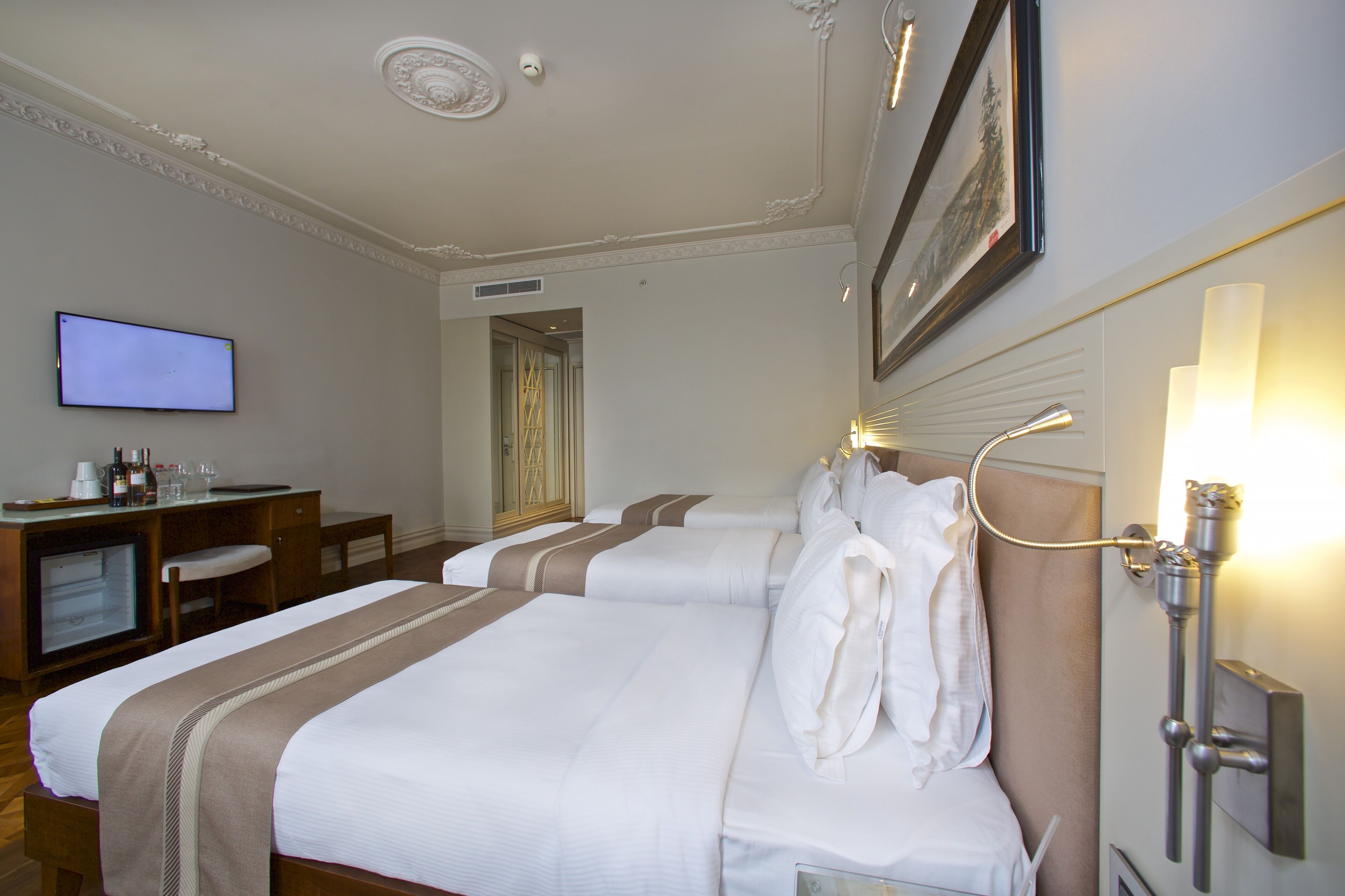 A hotel room with three beds, a desk with a television, and a bathroom with a shower.