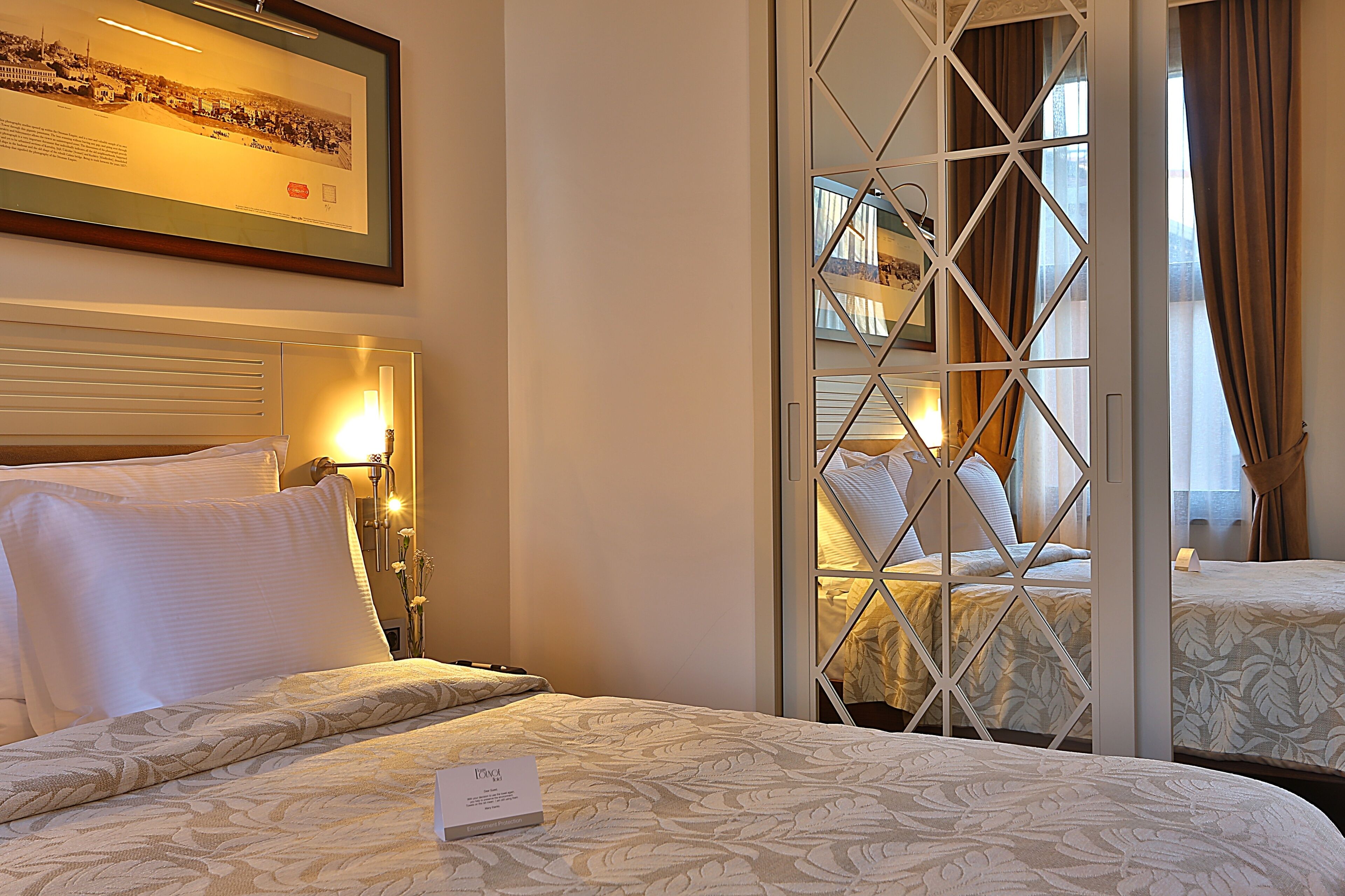 A hotel room with a bed, a nightstand, a framed picture on the wall, and a window with curtains.