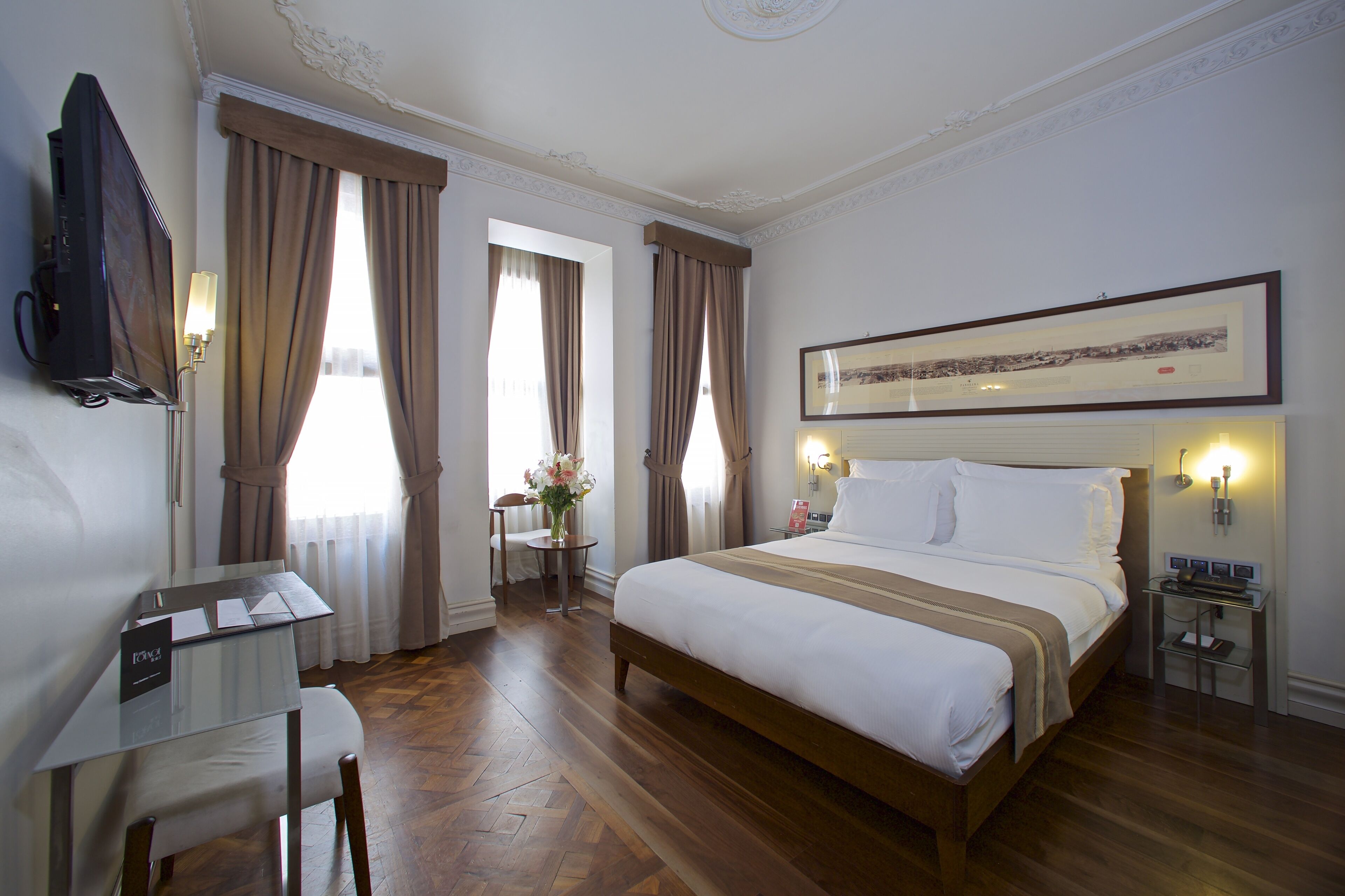 Una habitación de hotel con cama, escritorio, silla, televisor y un cuadro en la pared.