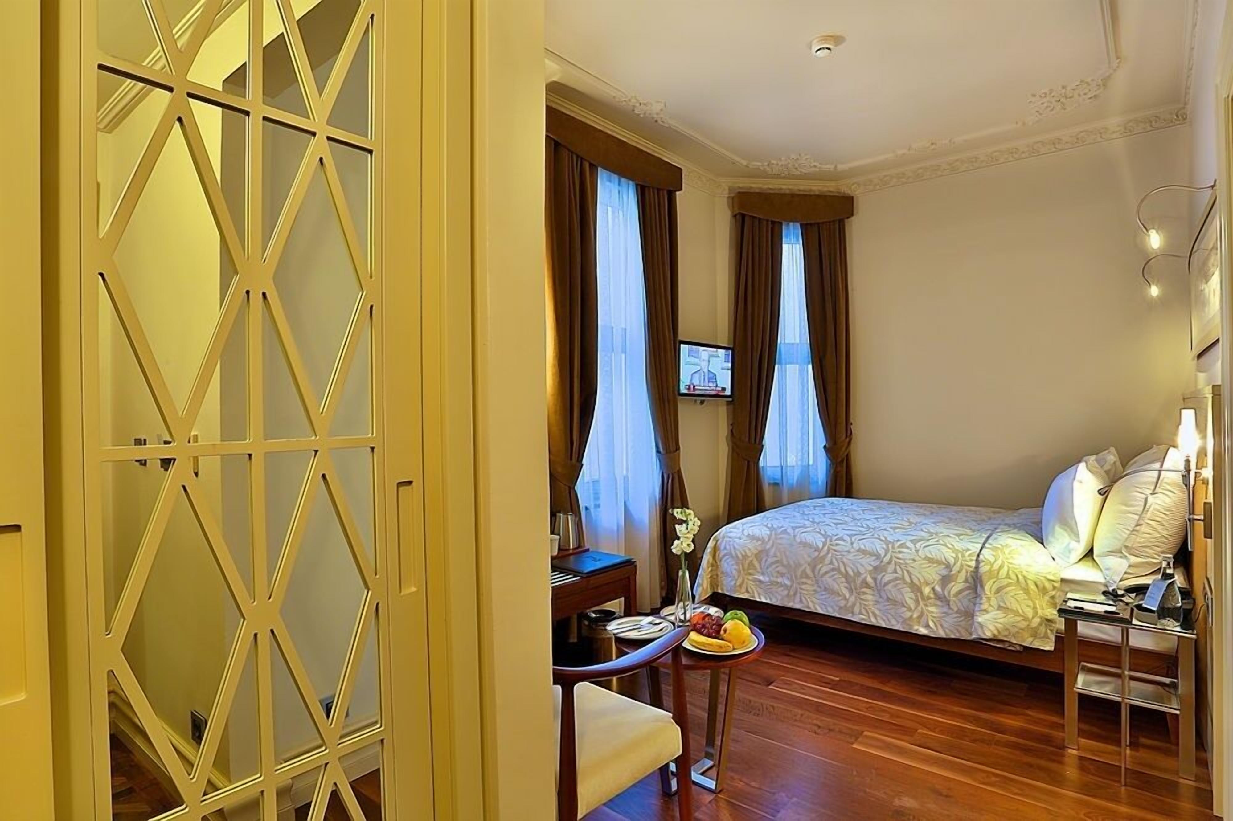 A hotel room with a bed, a desk, a chair, a small table with fruit, and a TV.