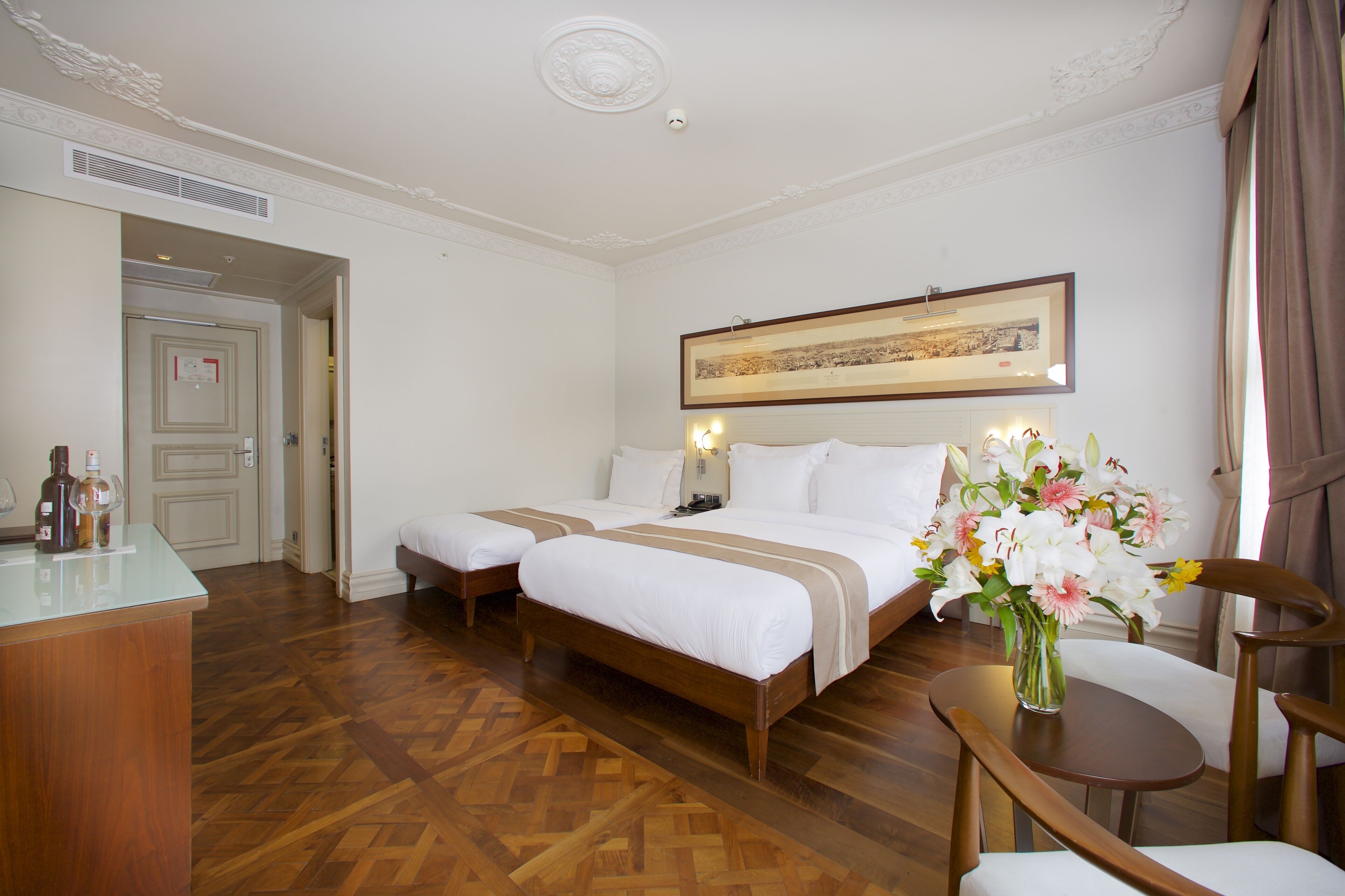 Camera d'albergo con due letti, una scrivania, una sedia, un vaso con fiori e un quadro appeso al muro.